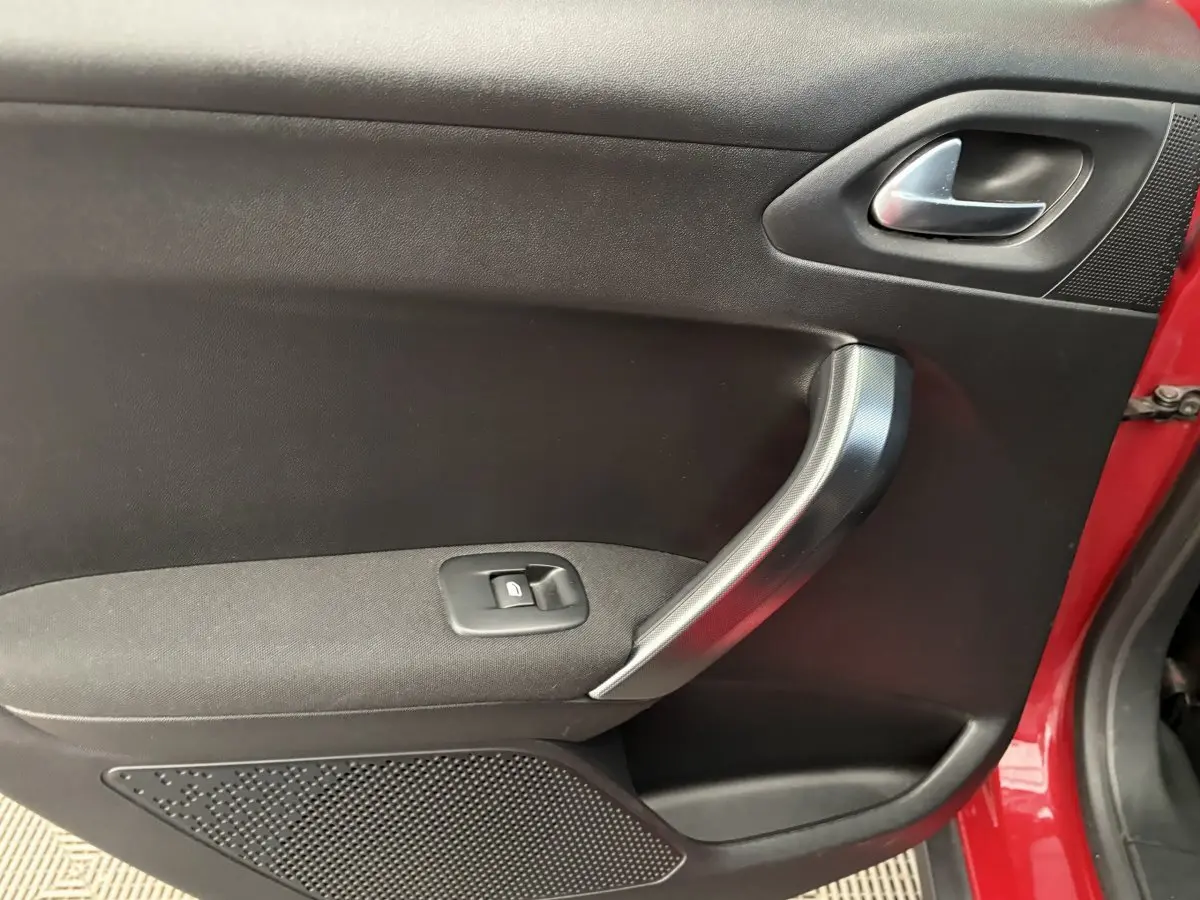 Gros plan sur la porte intérieure côté gauche d'une Peugeot 2008 rouge, avec poignée argentée et bouton de fenêtre électrique.