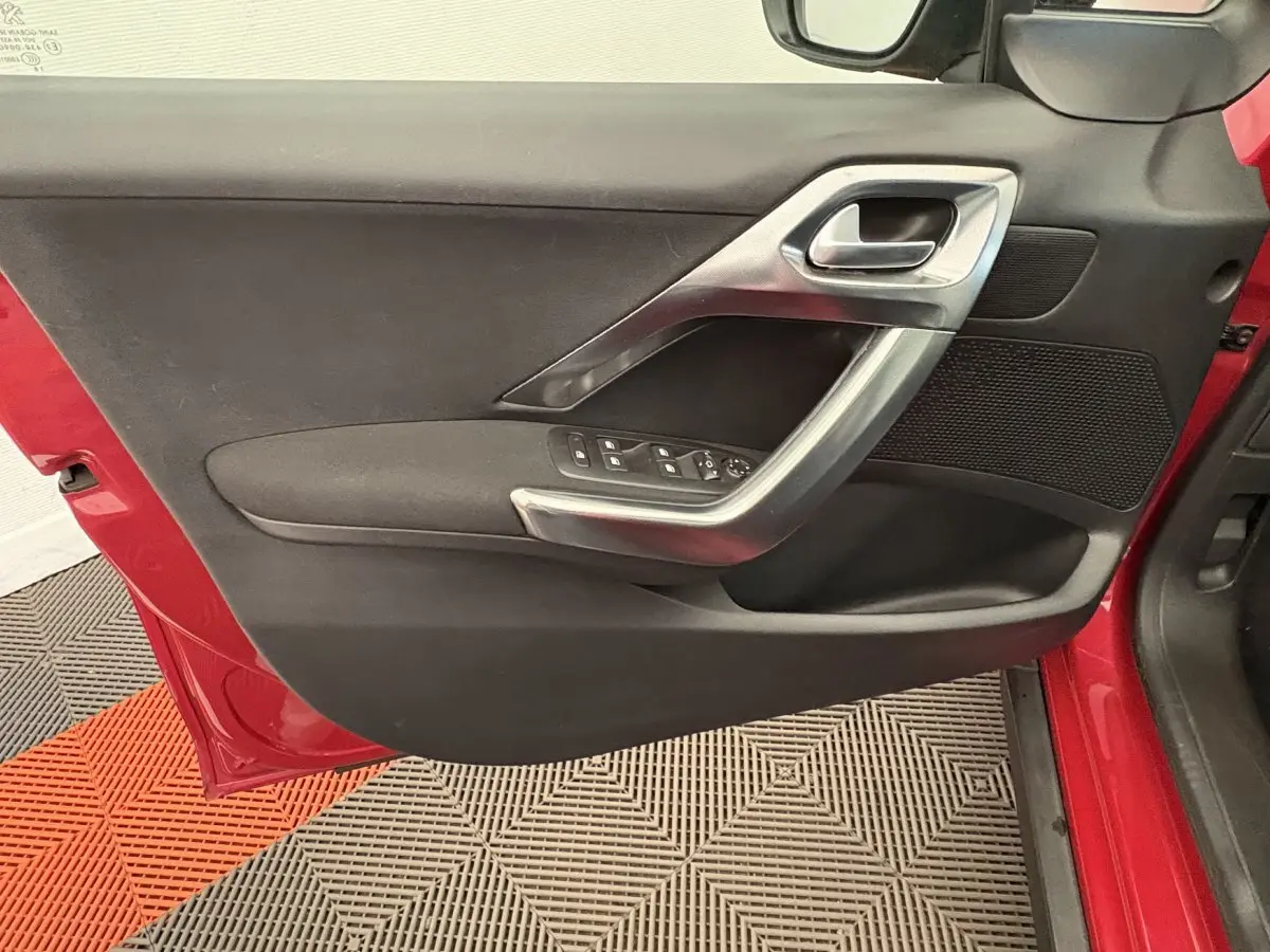 Vue rapprochée de la porte avant gauche rouge du Peugeot 2008 avec garniture noire et poignée argentée.