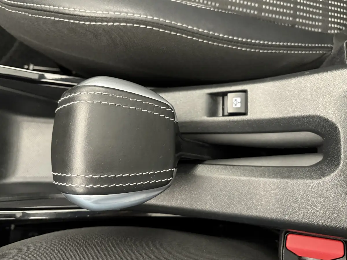 Gros plan sur le levier de vitesse en cuir noir avec surpiqûres blanches dans l'habitacle d'un Peugeot 2008 rouge.