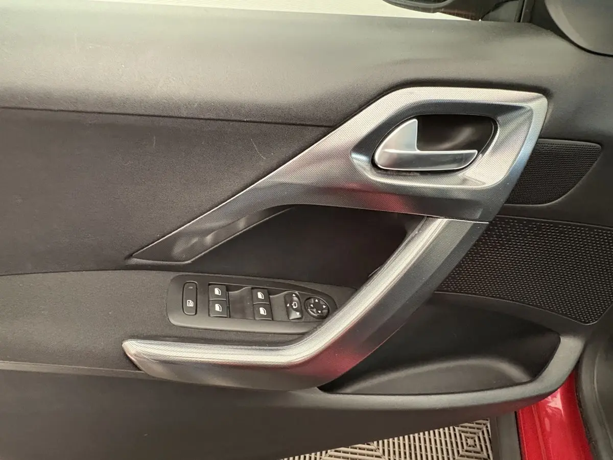 Vue rapprochée de la porte côté conducteur rouge du Peugeot 2008 avec commandes des vitres et poignée argentée.