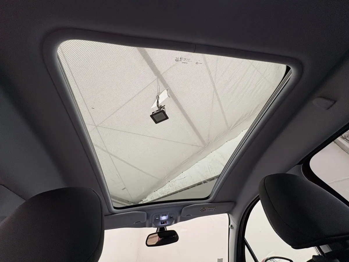 Toit panoramique vu de l'intérieur avant du Peugeot 2008 rouge, mettant en valeur le grand vitrage et les sièges noirs.