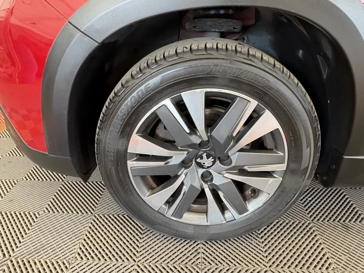 Gros plan sur la roue avant gauche rouge d’un Peugeot 2008 avec jante alliage et logo lion central.