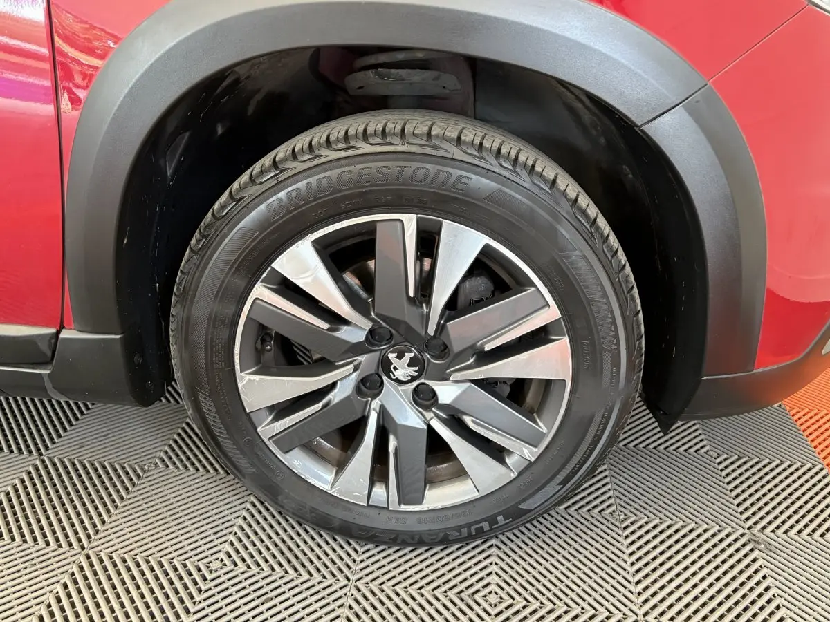 Gros plan sur la roue avant gauche d'un Peugeot 2008 rouge, mettant en valeur la jante alliage et le pneu Bridgestone.