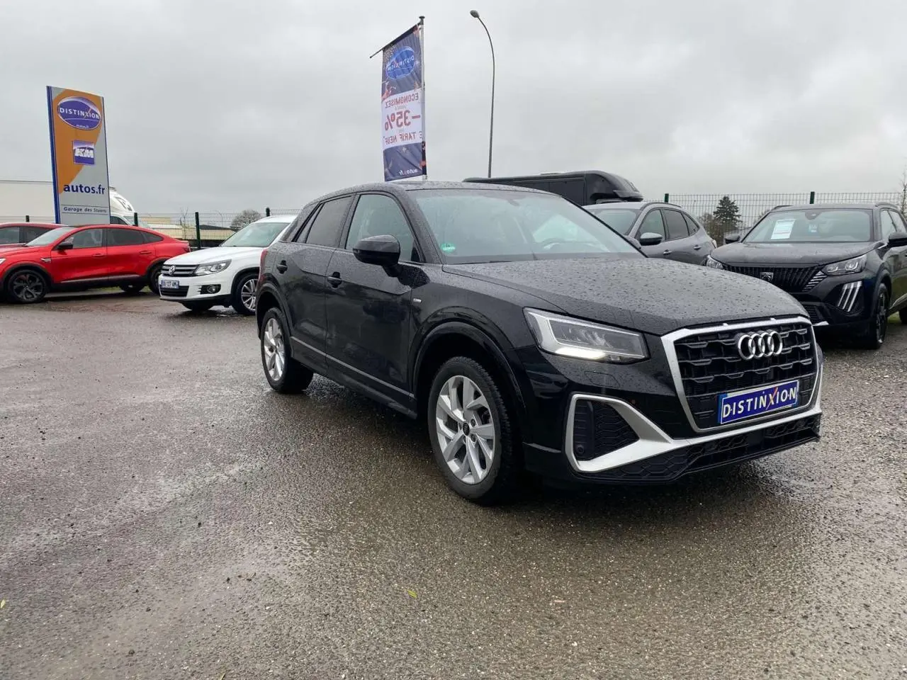 Audi Q2 noire vue en 3/4 avant droit sous la pluie, avec jantes alliage et calandre S line distinctive.