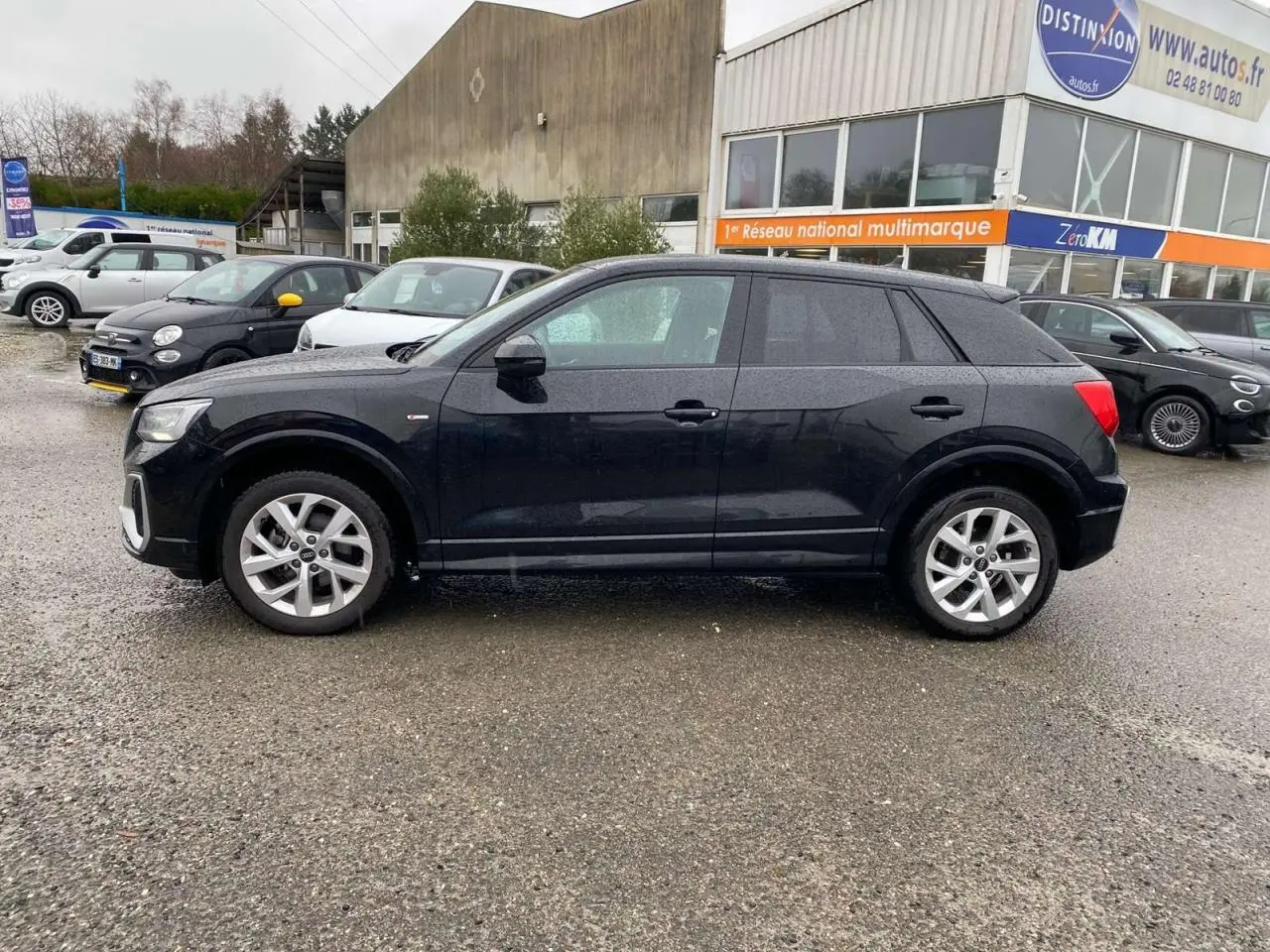 Audi Q2 noire vue de profil côté gauche, avec jantes alliage et carrosserie brillante sous la pluie.