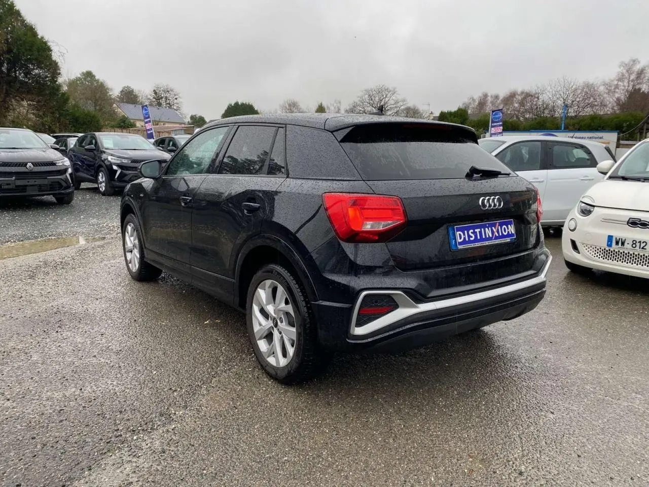 Audi Q2 noire vue 3/4 arrière droit sous la pluie, avec jantes alliage et feux arrière rouges visibles.
