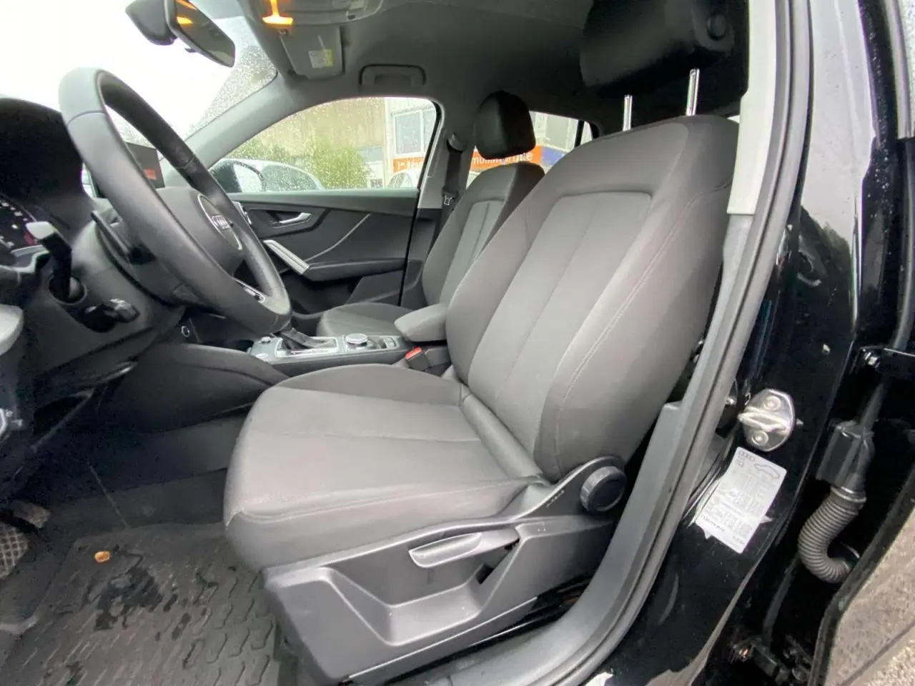 Vue intérieure côté conducteur d'un Audi Q2 noir 2023, sièges avant en tissu gris et tableau de bord visible.