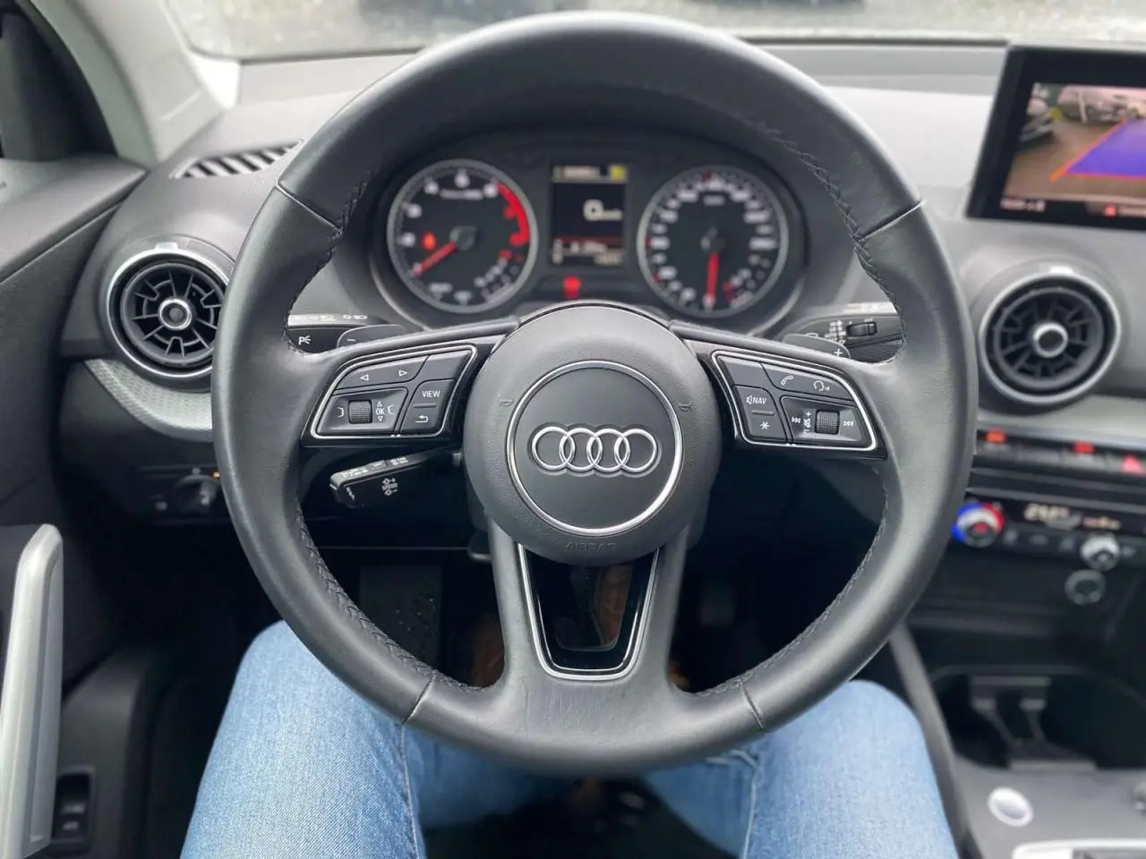 Vue centrée sur le volant noir de l'Audi Q2 2023, avec tableau de bord et écran de caméra de recul visibles.