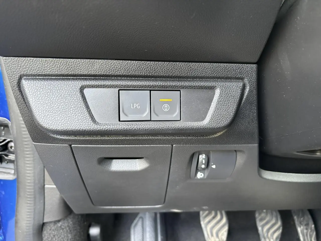 Détail intérieur côté gauche avec boutons LPG et verrouillage, plancher et pédales visibles, portière bleu Iron ouverte.