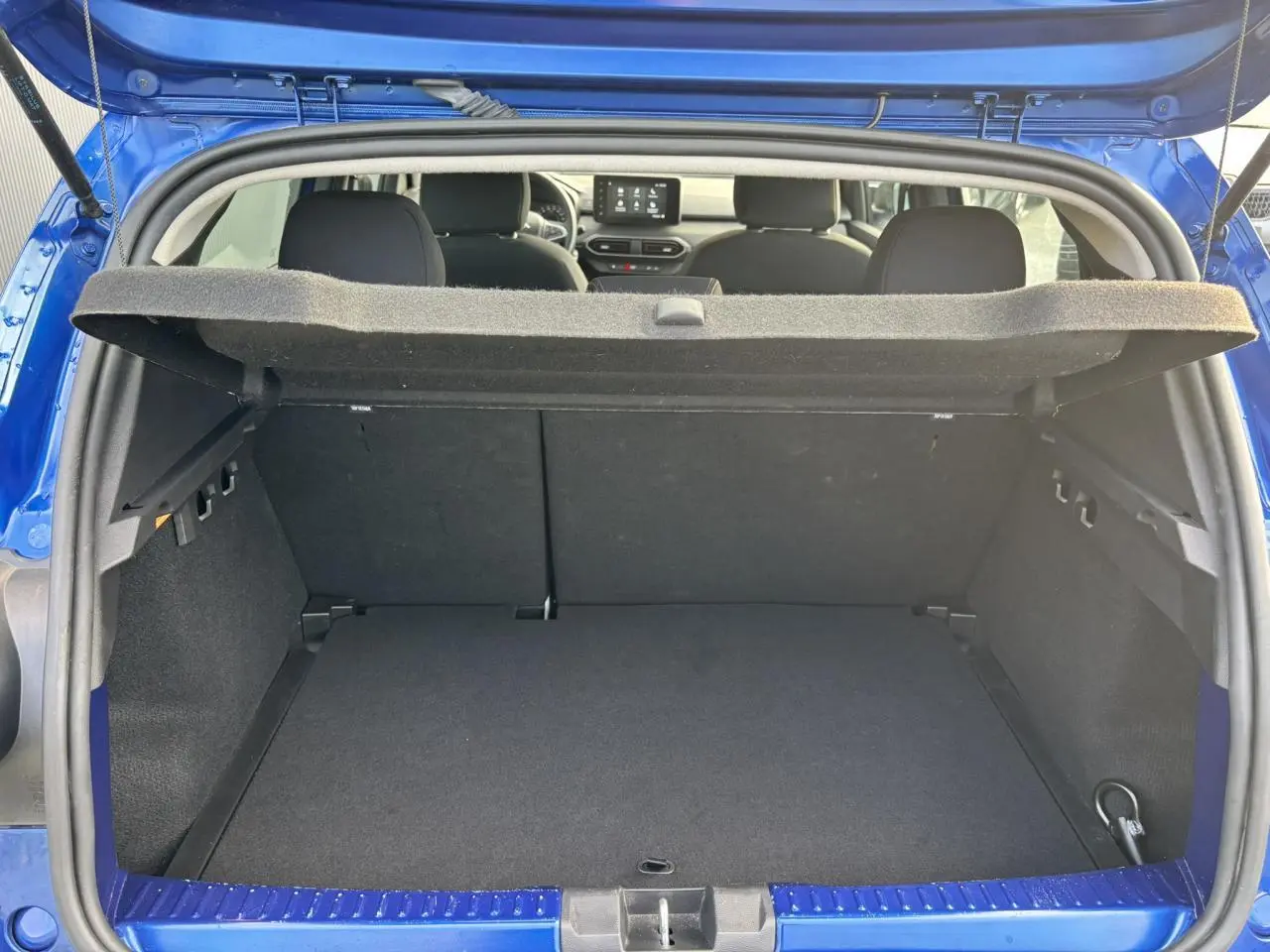 Coffre ouvert vu de l'arrière d'une Dacia Sandero Stepway Bleu Iron, intérieur noir et tableau de bord visible.