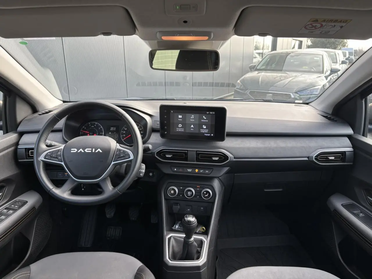 Vue intérieure avant du tableau de bord et volant de la Dacia Sandero Stepway Bleu Iron avec écran tactile et boîte manuelle.