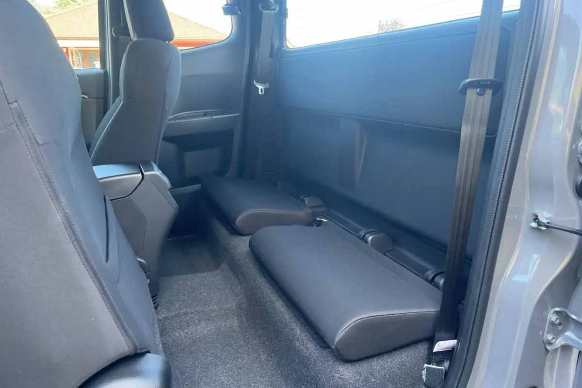 Vue intérieure arrière droite du pick-up Isuzu D-MAX 2026 gris Kinabalu avec sièges strapontins rabattus en tissu noir.