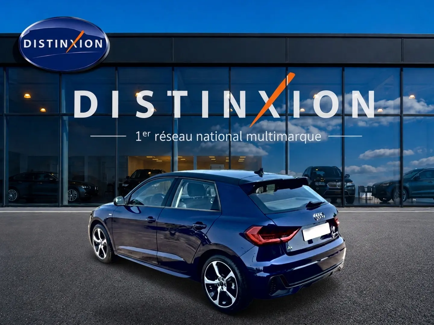 Audi A1 Sportback bleu foncé vue 3/4 arrière droit, avec jantes alu et becquet arrière visible devant showroom Distinxion.