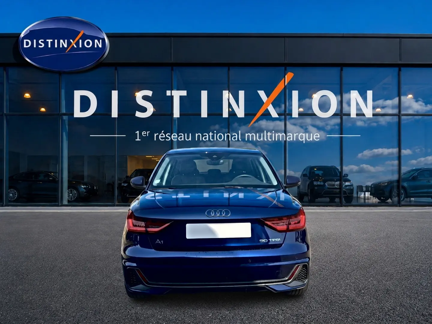 Vue arrière d'une Audi A1 Sportback 30 TFSI bleu foncé avec feux LED et becquet arrière, devant une vitrine Distinxion.