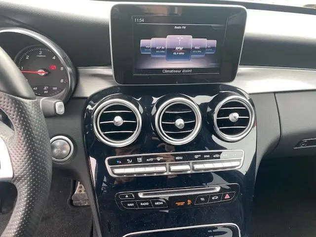 Vue rapprochée du tableau de bord central d'une Mercedes Classe C 250D 2018, avec écran multimédia et aérateurs ronds chromés.