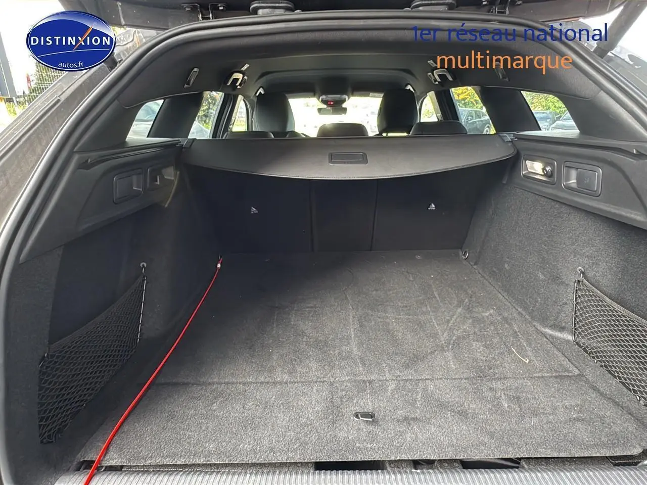 Coffre ouvert vu de l'arrière d'une Peugeot 308 SW PHEV 225 GT gris selenium avec filet de rangement latéral.
