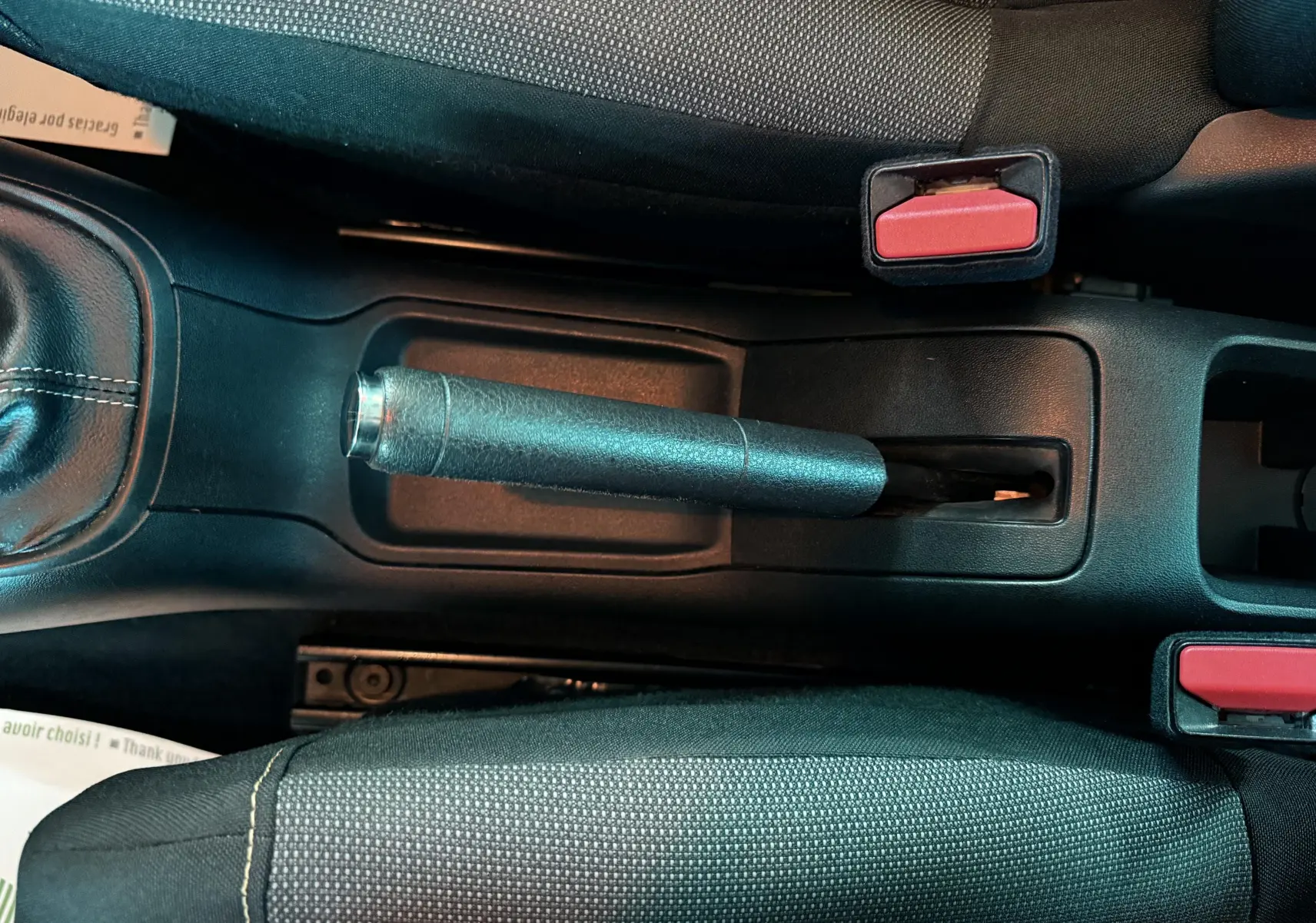 Vue plongeante sur le frein à main manuel et les sièges noirs de la Citroën C3 III 1.5 BHDI 100 de 2021.