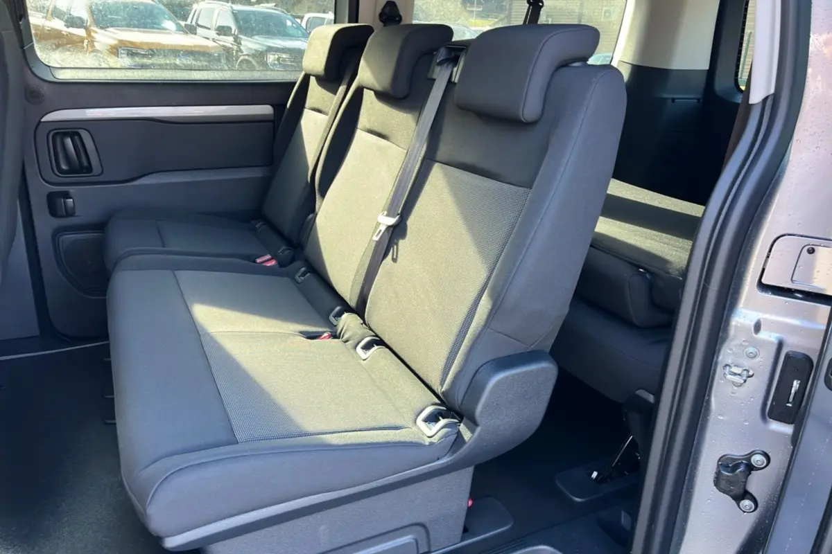 Vue intérieure côté droit du Peugeot Traveller gris acier 2025, montrant la banquette arrière trois places et la porte coulissante ouverte.