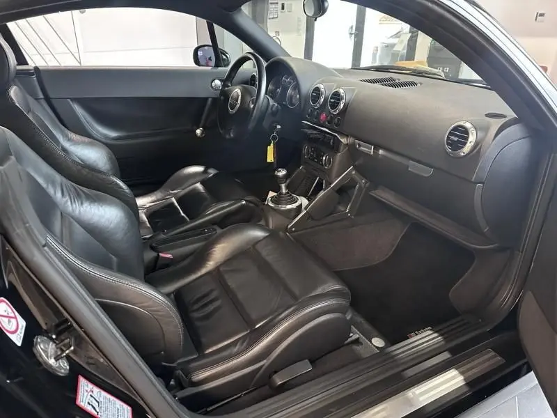Intérieur noir de l'Audi TT Coupé 2002 vu côté conducteur, avec sièges sport en cuir et levier de vitesse manuel.