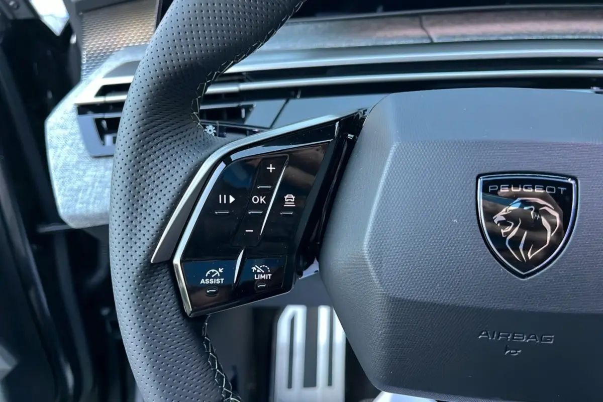 Gros plan sur le volant cuir perforé du Peugeot 5008 Hybrid 145 GT Alcantara avec commandes multifonctions et logo lion noir.