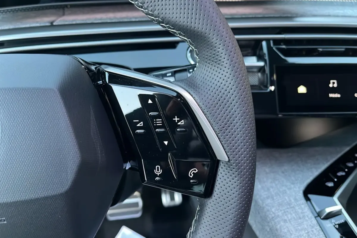 Gros plan sur le volant cuir perforé du Peugeot 5008 Hybrid 145 GT avec commandes multifonctions et tableau de bord numérique.