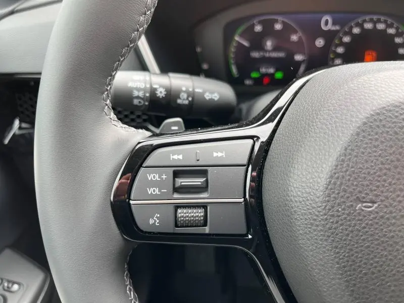 Gros plan sur les commandes audio et volume au volant cuir noir du Honda CR-V 2024, avec tableau de bord flou en arrière-plan.