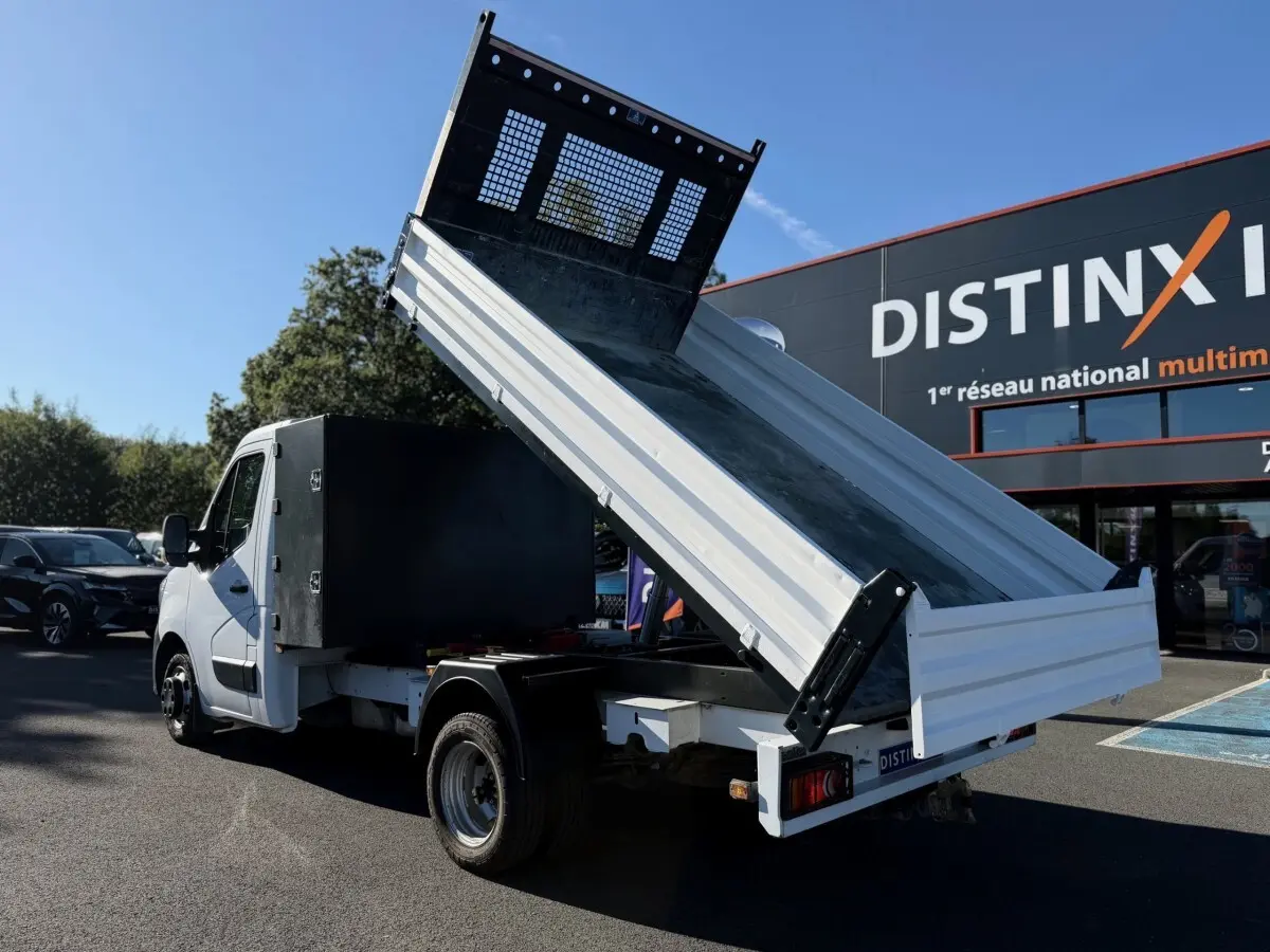 Renault Master blanc vu en 3/4 arrière avec benne relevée et grand coffre noir sur parking extérieur.