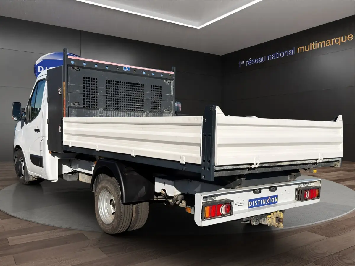 Renault Master blanc vue 3/4 arrière avec benne et ridelles blanches en intérieur showroom.