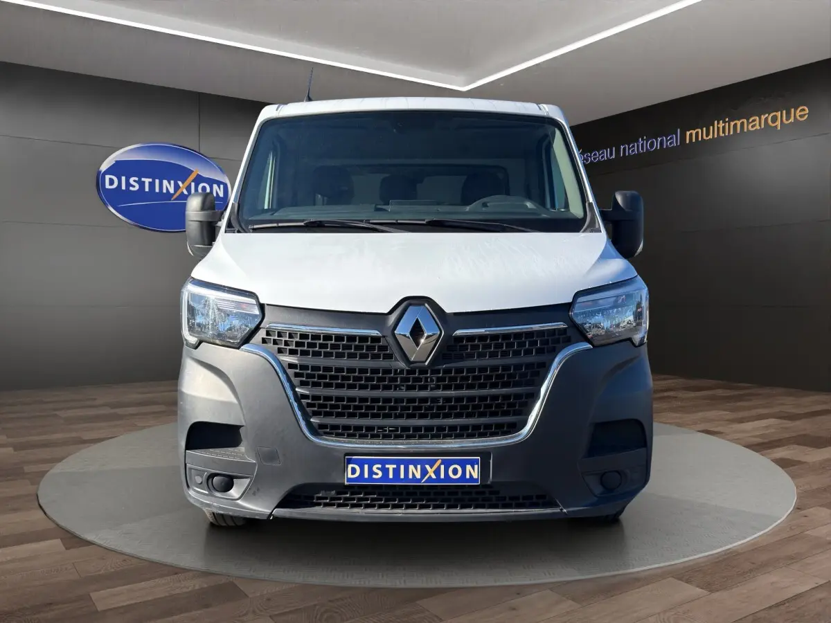 Vue avant d’un utilitaire Renault Master blanc avec calandre noire et logo Renault bien visible, sur fond intérieur showroom.