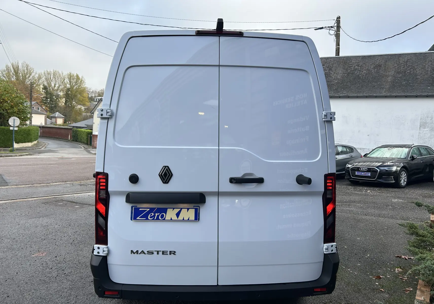 Vue arrière d’un fourgon Renault Master blanc avec portes battantes et logo noir, stationné en extérieur.