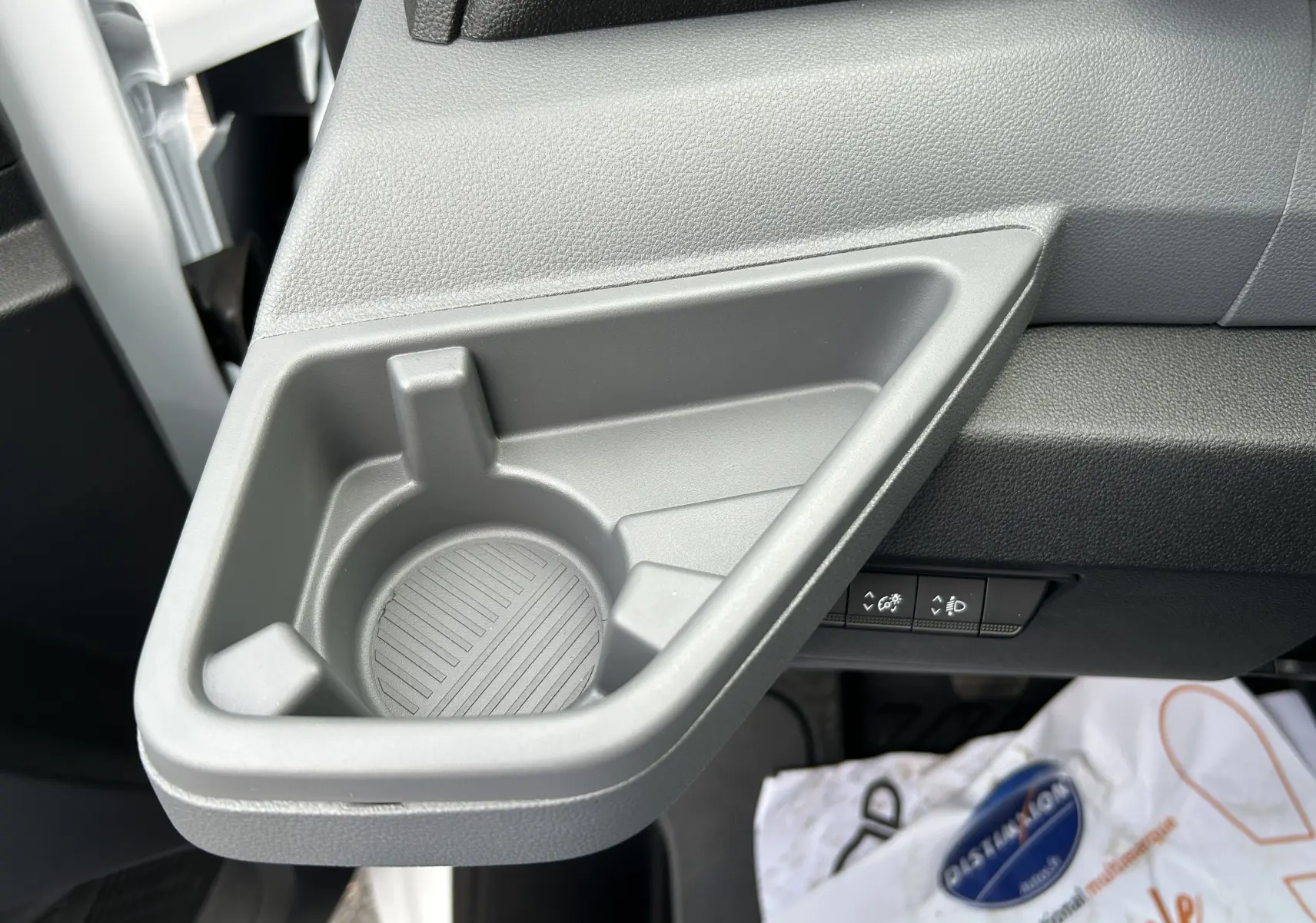 Gros plan sur le porte-gobelet gris intégré côté passager du Renault Master blanc, avec commandes de réglage en arrière-plan.