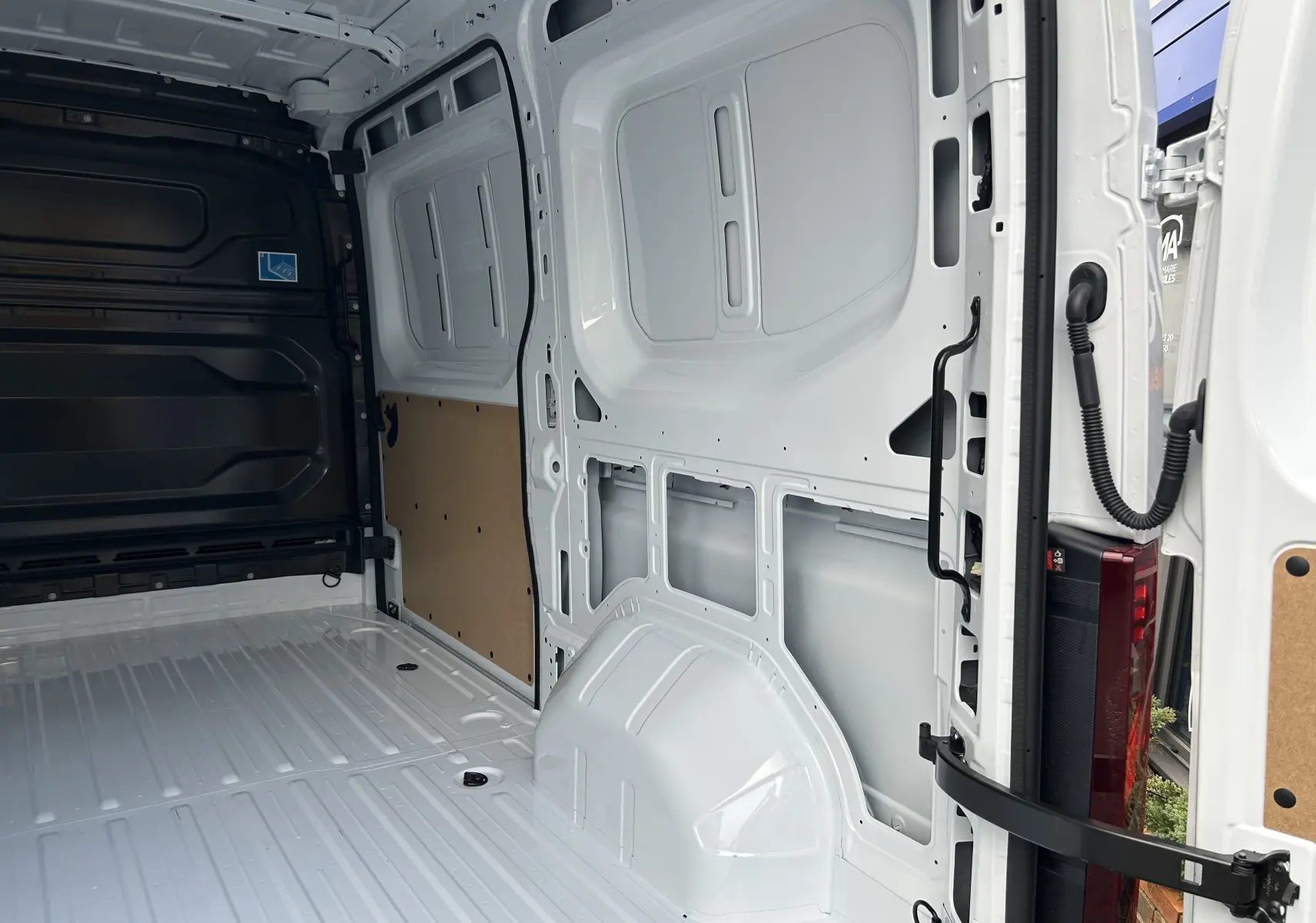 Vue intérieure arrière du fourgon Renault Master blanc, montrant l’espace de chargement vide avec parois métalliques et panneau bois.