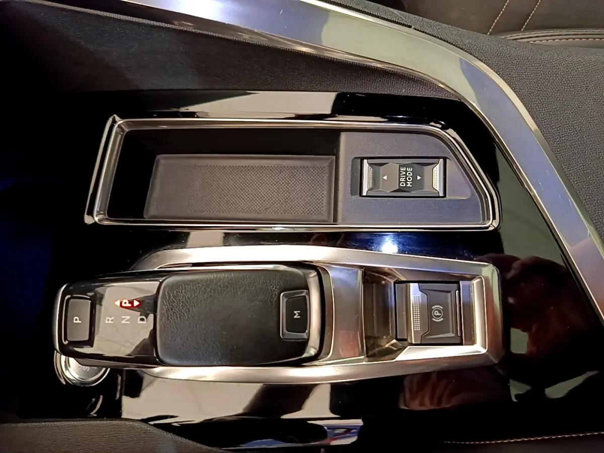 Gros plan sur la console centrale noire brillante du Peugeot 3008 rouge avec levier de boîte auto et bouton Drive Mode.