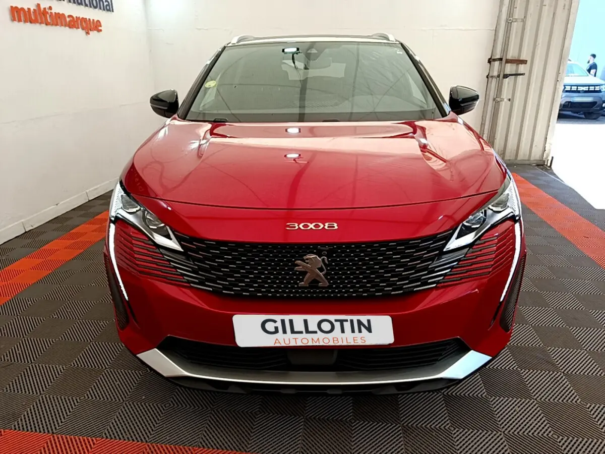 Vue frontale d'un Peugeot 3008 rouge brillant avec calandre noire et logo lion central sur fond de showroom.
