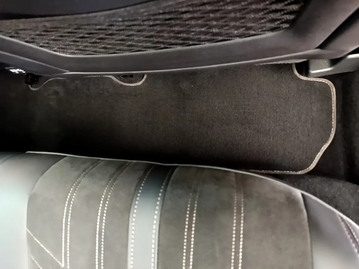 Gros plan sur le tapis de sol et l'assise en cuir noir avec surpiqûres blanches côté passager du Peugeot 3008 GT rouge.