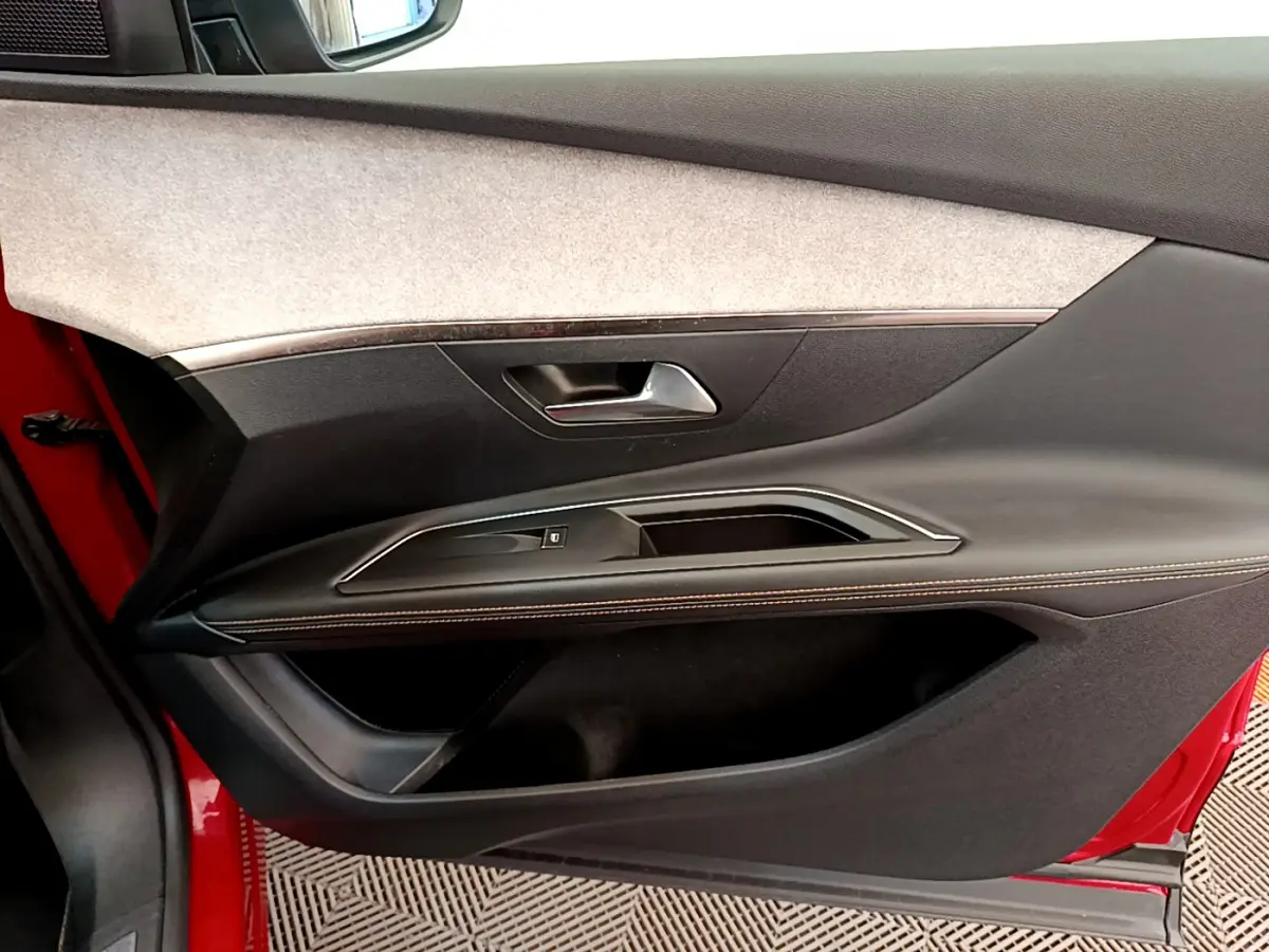 Vue côté gauche de la porte avant rouge du Peugeot 3008 GT avec garniture noire et surpiqûres orange.