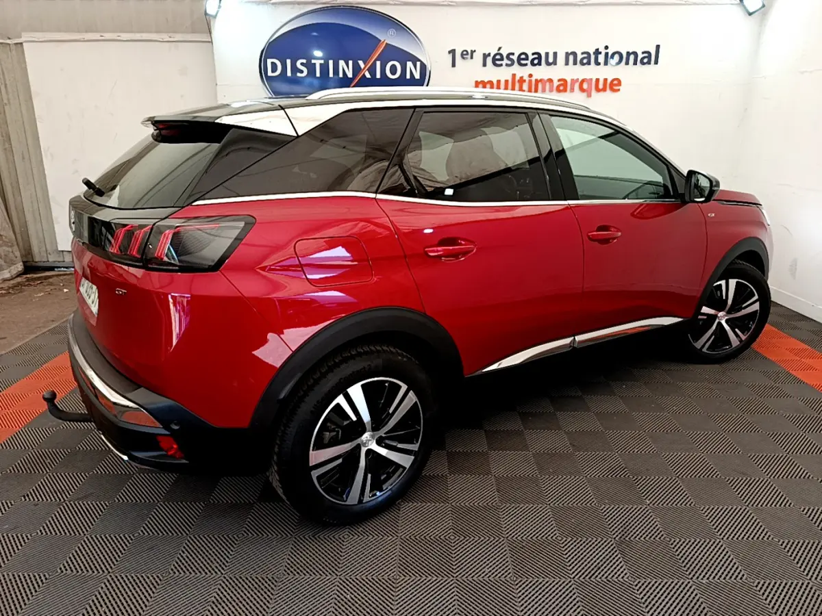 Vue 3/4 arrière droite d'un Peugeot 3008 GT rouge avec jantes alliage et toit noir dans un showroom.