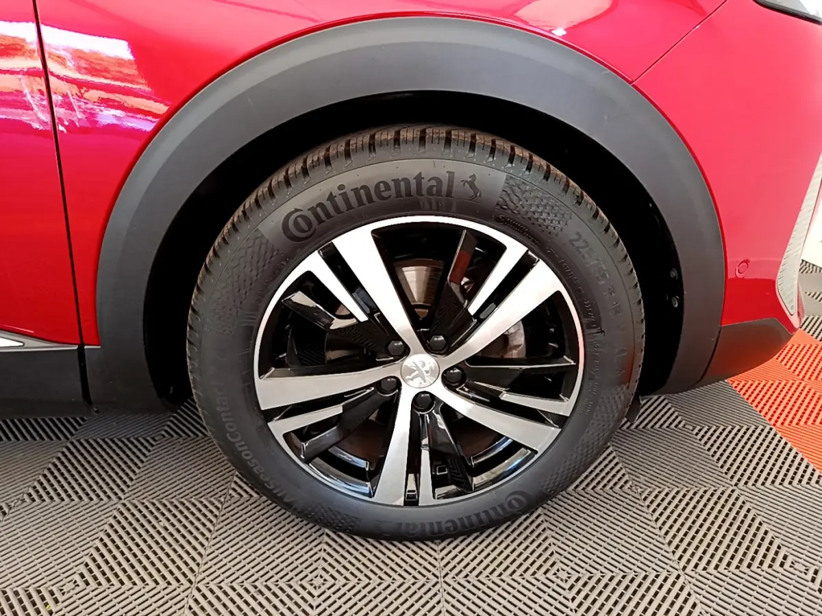 Gros plan sur la roue avant gauche d'un Peugeot 3008 rouge, jante alliage bicolore et pneu Continental.