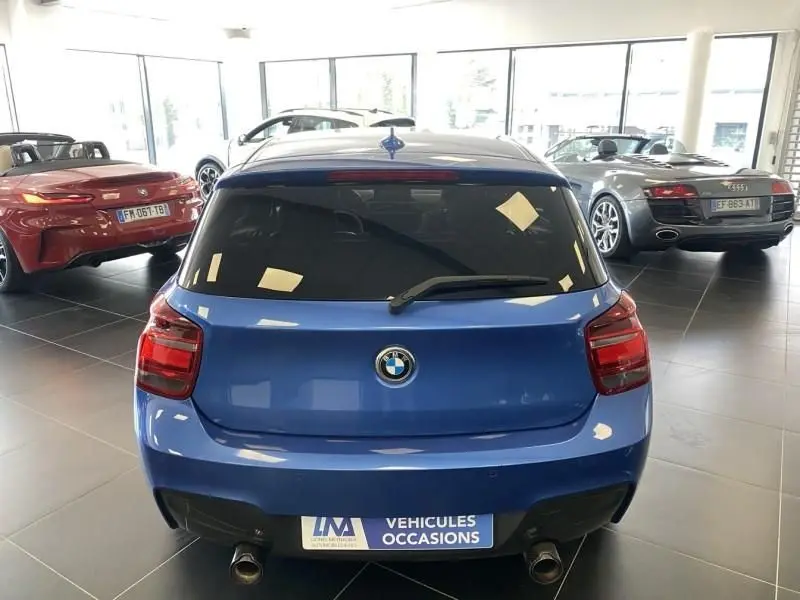 Vue arrière d'une BMW Série 1 135 i 320CV bleu métal 2013 dans un showroom avec échappements doubles visibles.