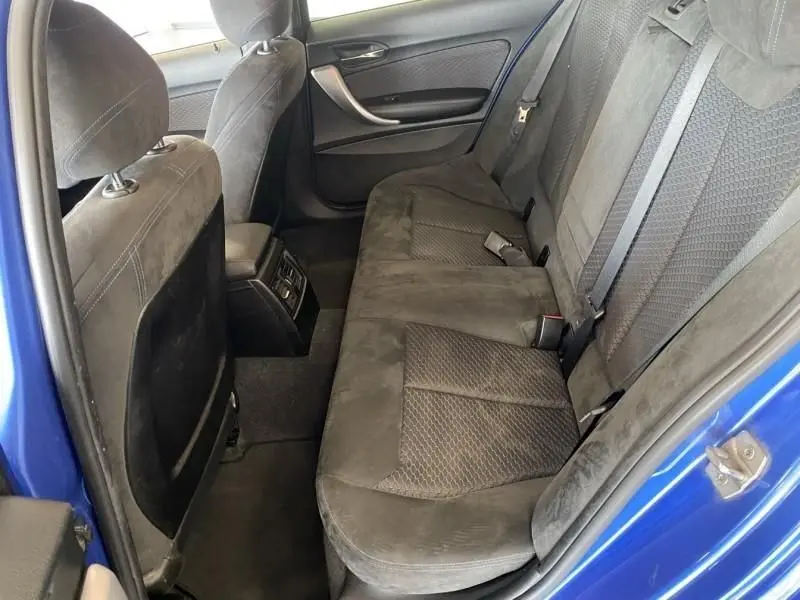 Vue intérieure arrière gauche montrant les sièges en tissu noir et la portière bleu métal d'une BMW Série 1 135i 2013.