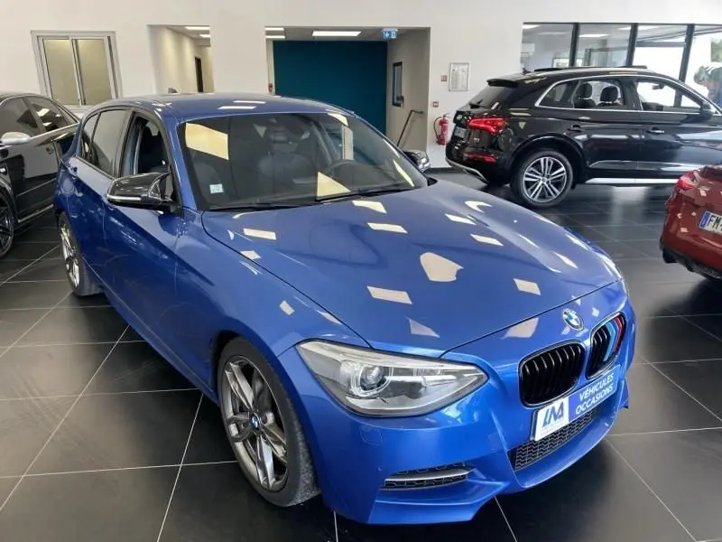 BMW Série 1 135 i bleu métal vue 3/4 avant droit en showroom avec calandre M et jantes sport