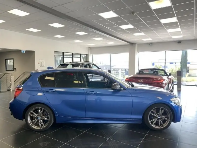 Profil côté gauche d'une BMW Série 1 135 i 320CV M bleu métal, exposée en intérieur lumineux avec jantes sport.