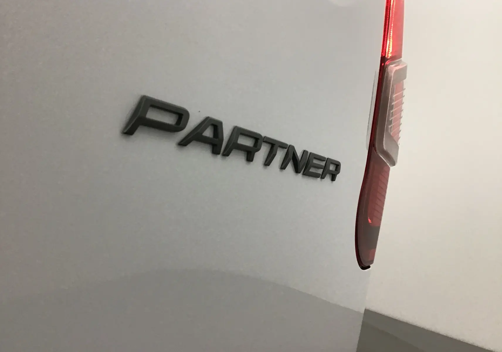 Gros plan sur l'arrière droit blanc du Peugeot Partner avec le logo "PARTNER" et le feu arrière vertical rouge.