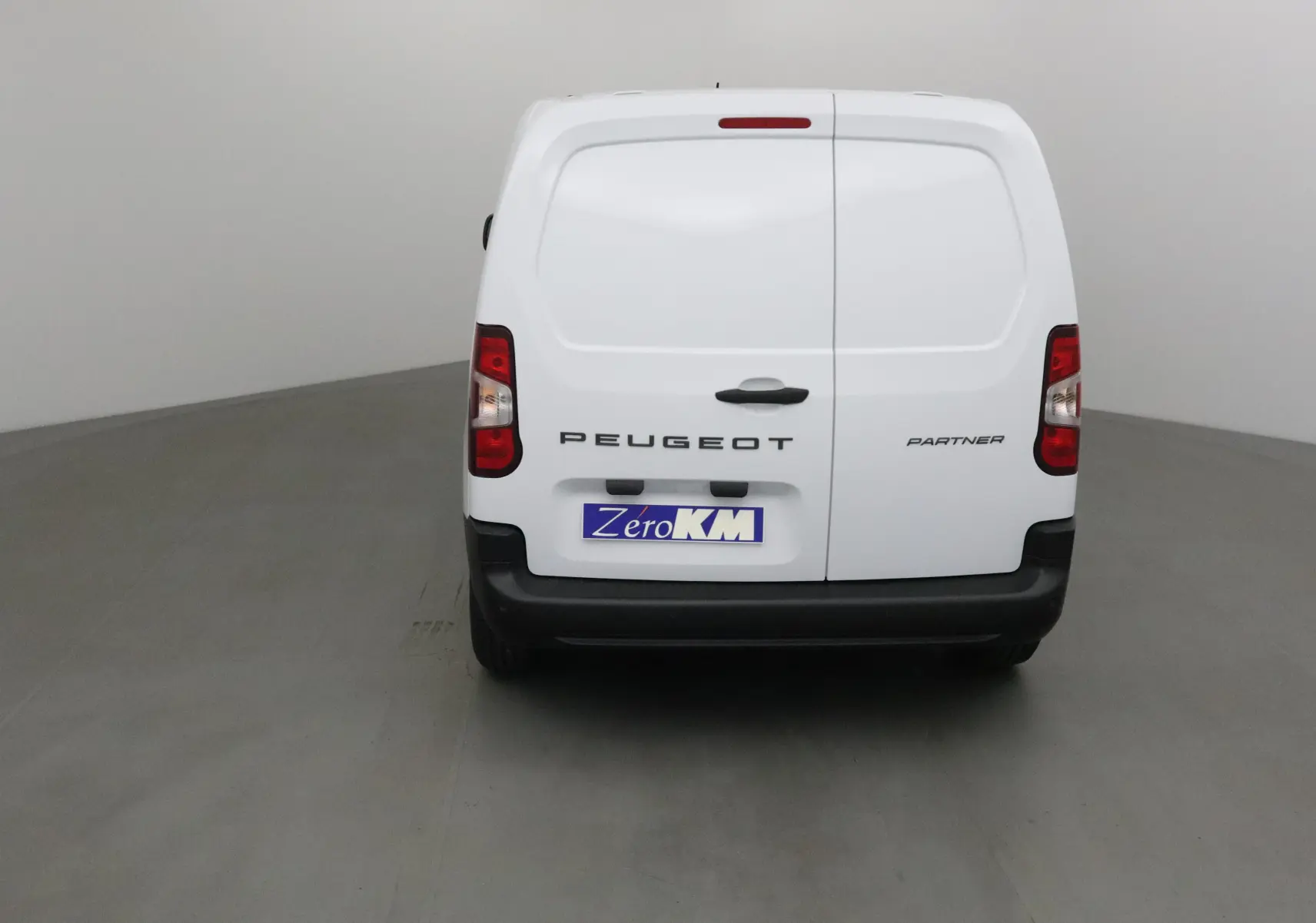 Vue arrière d'un utilitaire blanc Peugeot Partner avec portes battantes et plaque ZeroKM visible.