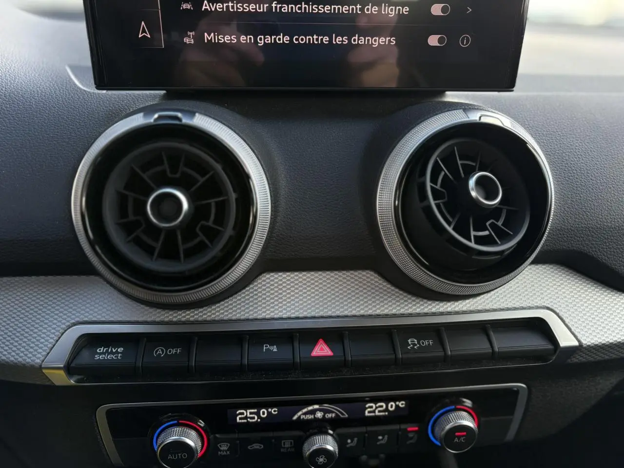 Détail du tableau de bord de l'Audi Q2 30 TDI S-Line 2025, montrant les aérateurs ronds et la commande de climatisation automatique bizona.