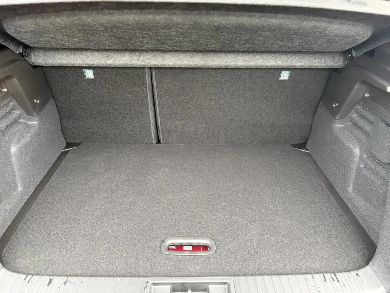 Coffre ouvert du Renault Captur rouge Flamme, vue intérieure montrant le plancher de coffre mobile et les côtés en tissu gris.