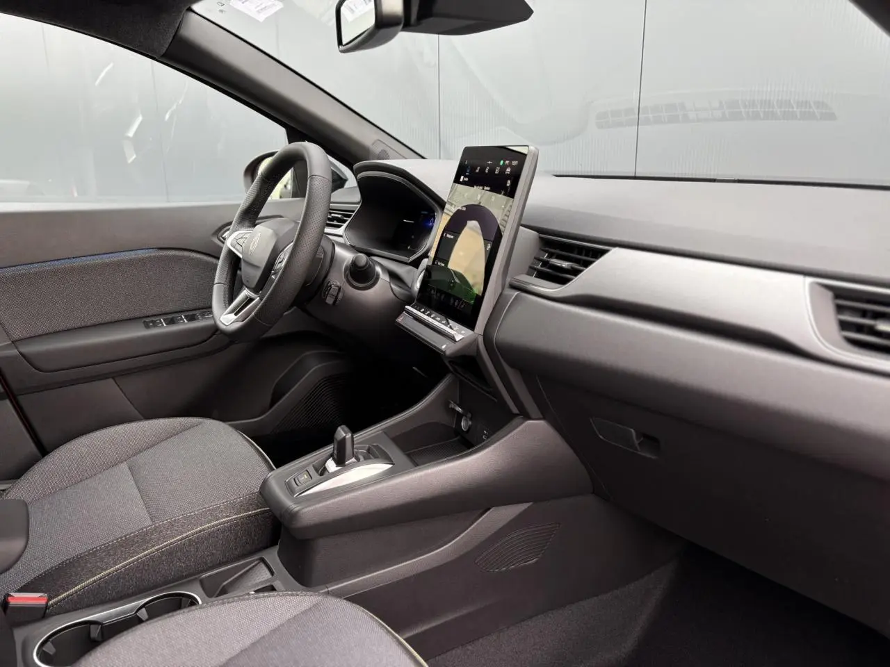 Vue intérieure côté conducteur du Renault Captur 2026, tableau de bord moderne avec écran tactile vertical et sièges tissu gris.