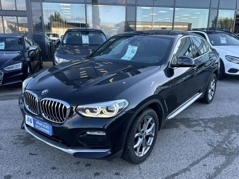BMW X4 X Drive 190 CV X-Line gris foncé vue 3/4 avant avec calandre chromée et phares allumés