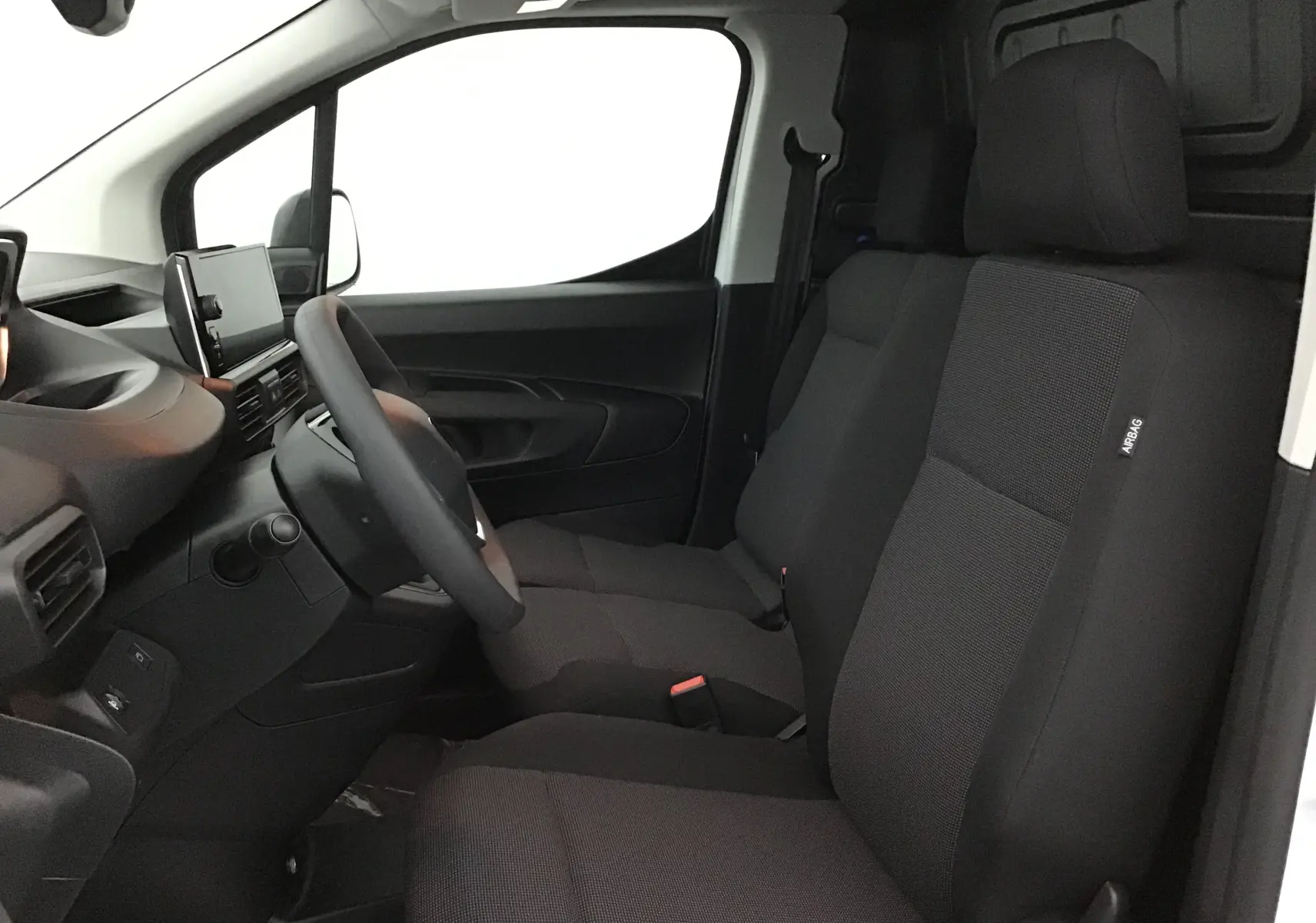 Vue intérieure côté conducteur du Peugeot Partner blanc, montrant les sièges avant et le tableau de bord moderne.