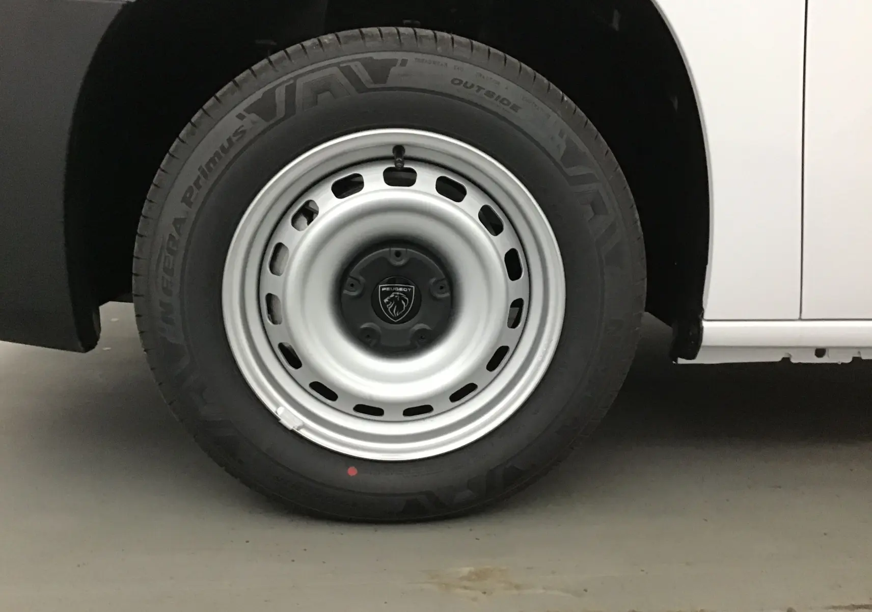 Gros plan sur la roue avant droite du Peugeot Partner blanc, jante acier avec logo lion au centre.